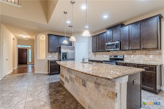 kitchen with sink, appliances with stainless steel finishes, hanging light fixtures, dark brown cabinets, and an island with sink