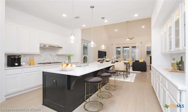 kitchen featuring white cabinets, ventilation hood, light hardwood / wood-style flooring, and a kitchen island with sink