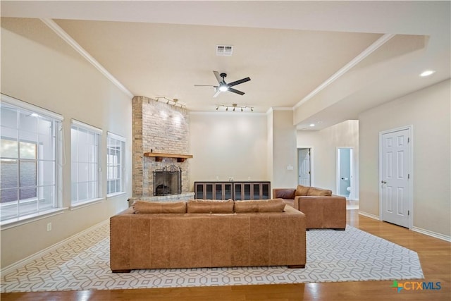 living room featuring light hardwood / wood-style flooring, rail lighting, ceiling fan, ornamental molding, and a large fireplace