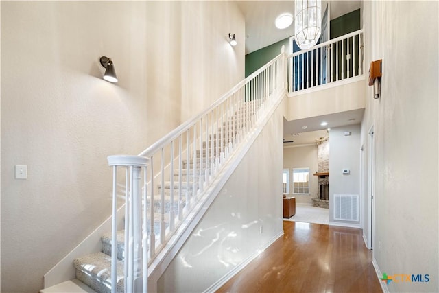 stairway with a high ceiling, a chandelier, hardwood / wood-style floors, and a fireplace