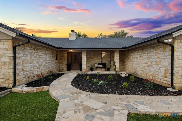 701 W Esparada Dr, Georgetown, TX 78628 - exterior entry at dusk with stone siding, a shingled roof, a porch, and a chimney
