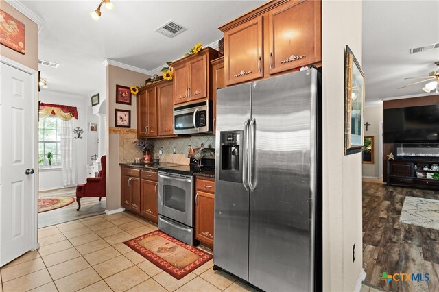 2307 Scott Dr, Copperas Cove, TX 76522 - kitchen with stainless steel appliances, brown cabinetry, dark countertops, ornamental molding, and decorative backsplash