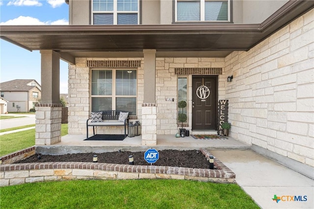 doorway to property with covered porch, stone siding, and stucco siding