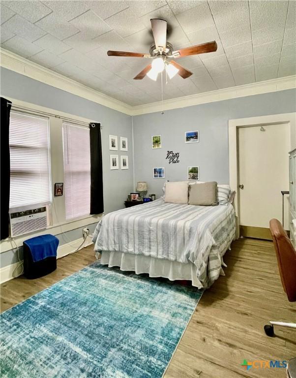 bedroom featuring a ceiling fan, crown molding, baseboards, and wood finished floors