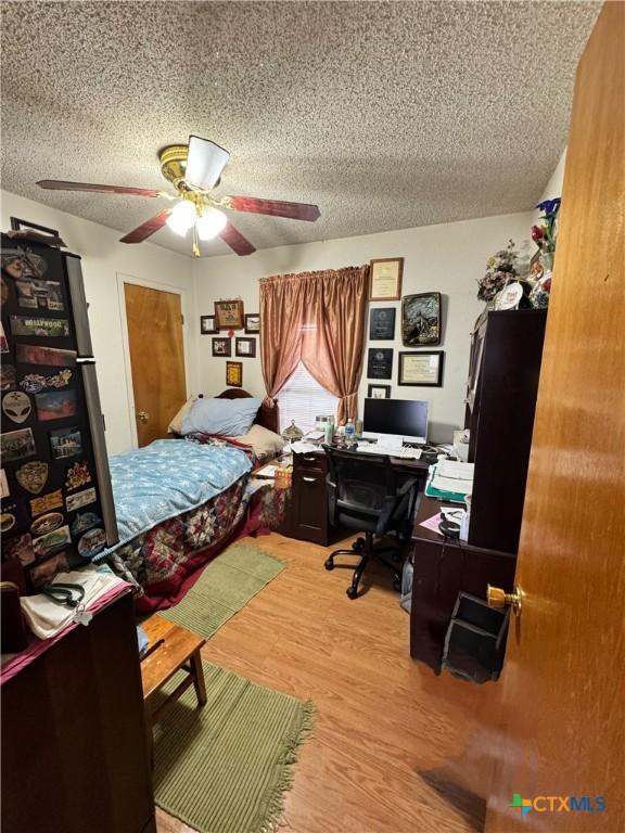 bedroom with ceiling fan, wood-type flooring, and a textured ceiling