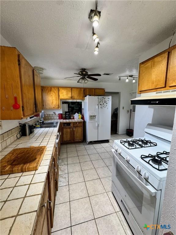 kitchen with tile countertops, ceiling fan, white appliances, a textured ceiling, and sink