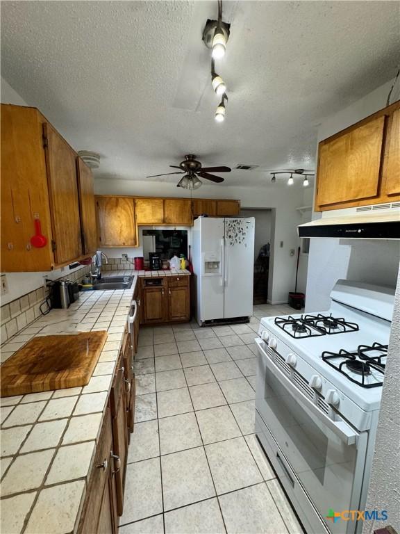 kitchen with ceiling fan, tile counters, white appliances, a textured ceiling, and sink