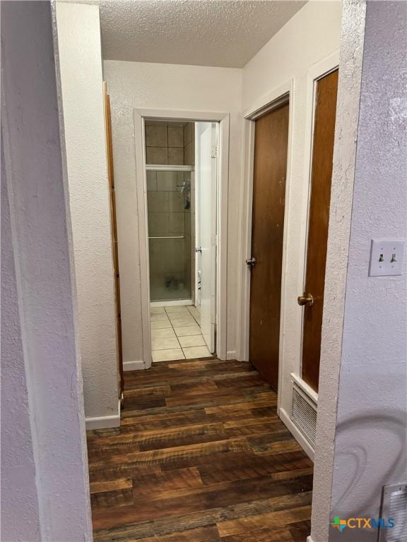 hallway with a textured ceiling and dark hardwood / wood-style floors