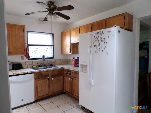 kitchen featuring ceiling fan, tile countertops, sink, white appliances, and light tile patterned flooring