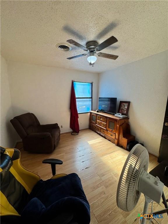 living room featuring ceiling fan, a textured ceiling, and light hardwood / wood-style flooring