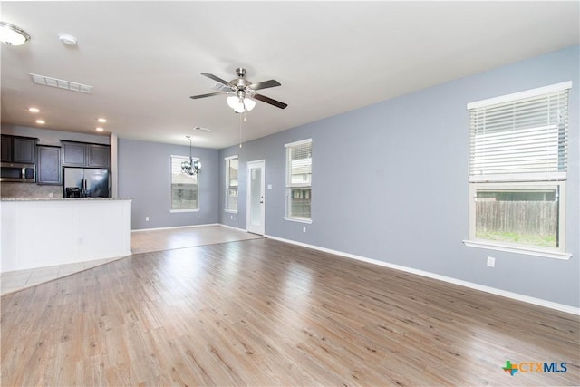 unfurnished living room featuring light wood-type flooring, baseboards, and ceiling fan with notable chandelier