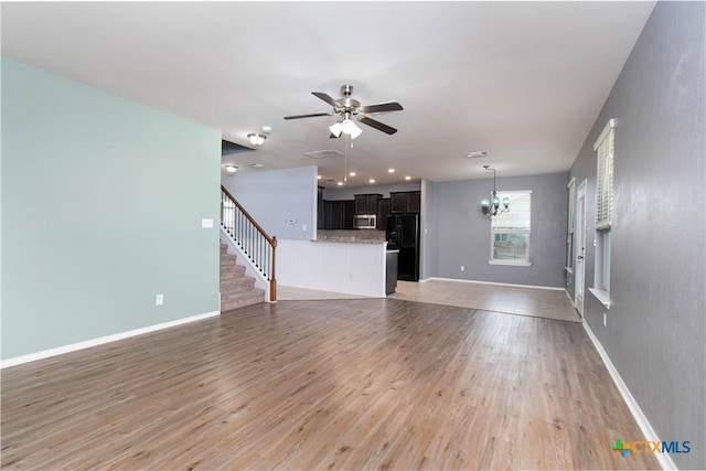 unfurnished living room with baseboards, light wood-type flooring, ceiling fan with notable chandelier, and stairway