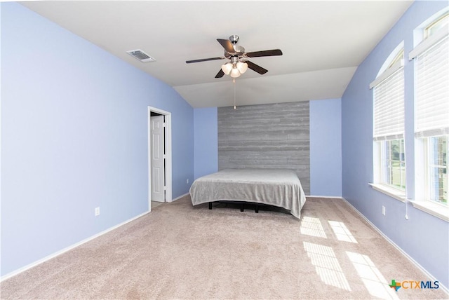 carpeted bedroom with lofted ceiling, an accent wall, visible vents, baseboards, and a ceiling fan