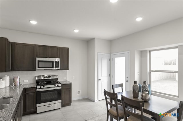 kitchen with light tile patterned flooring, decorative backsplash, light stone counters, stainless steel appliances, and dark brown cabinets