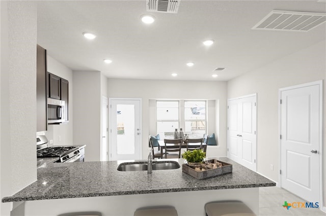 kitchen with sink, a kitchen bar, dark stone counters, kitchen peninsula, and stainless steel appliances