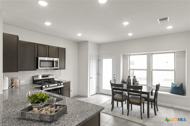 kitchen with appliances with stainless steel finishes, stone countertops, decorative backsplash, light tile patterned floors, and dark brown cabinets