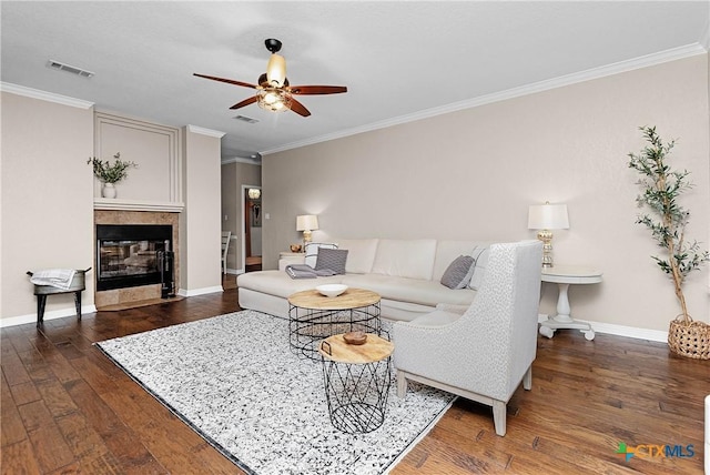 living area with visible vents, hardwood / wood-style floors, ornamental molding, a tile fireplace, and baseboards