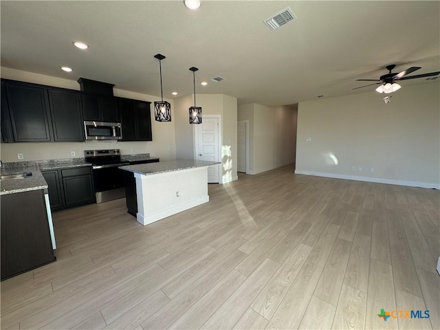 kitchen featuring light stone counters, stainless steel appliances, visible vents, a kitchen island, and dark cabinets