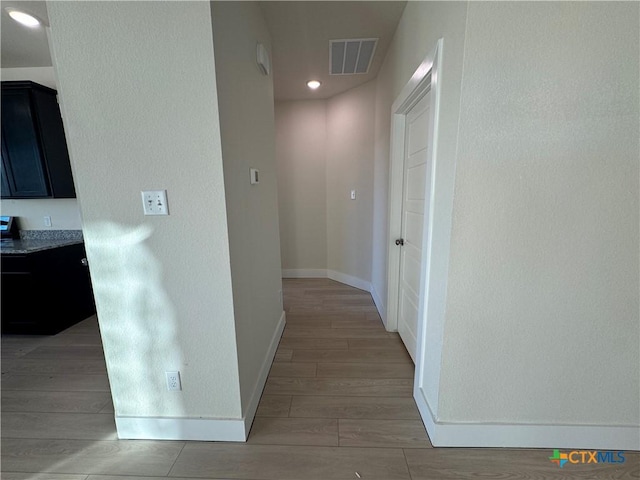 corridor featuring light wood finished floors, recessed lighting, visible vents, and baseboards