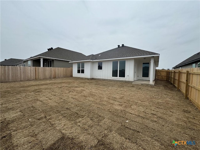 back of house with a fenced backyard, roof with shingles, board and batten siding, and a yard