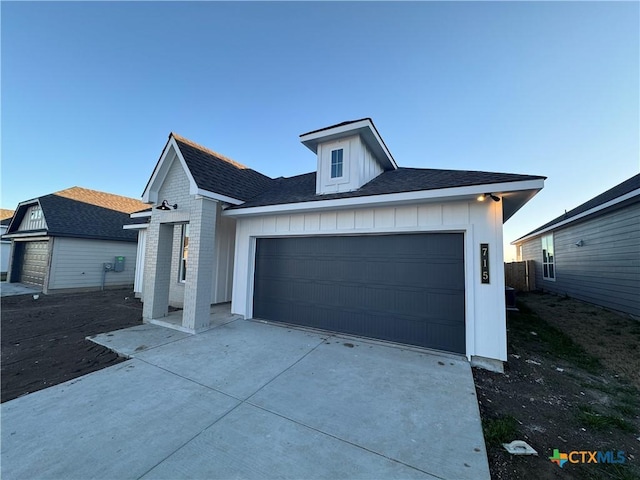 view of front of property featuring driveway, brick siding, board and batten siding, and an attached garage