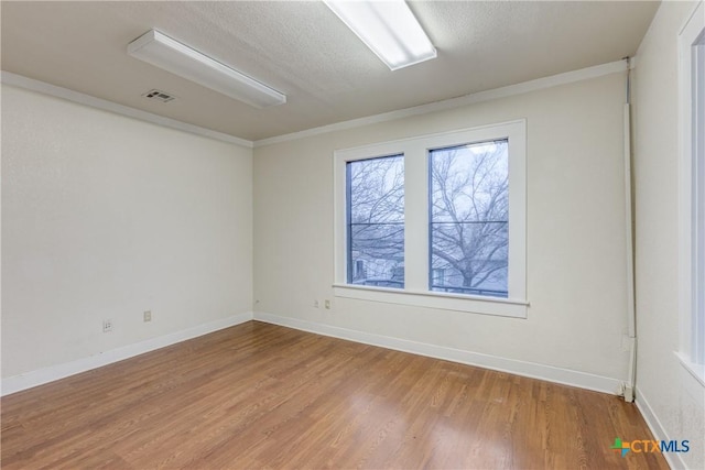 empty room with visible vents, a textured ceiling, baseboards, and wood finished floors