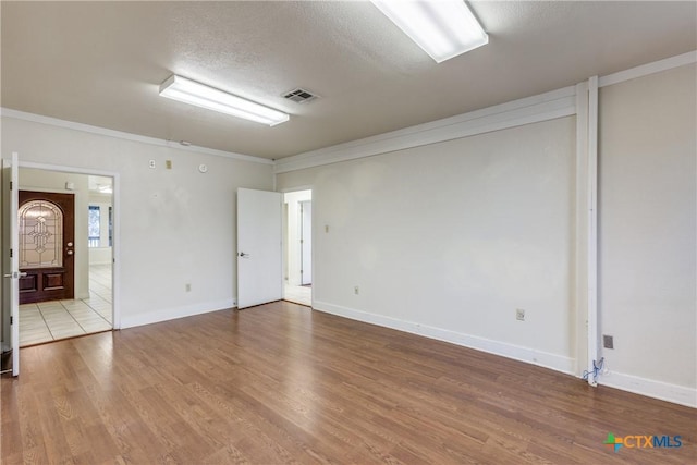 spare room featuring crown molding, visible vents, light wood-style flooring, a textured ceiling, and baseboards