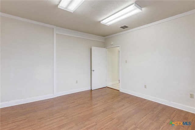 empty room with ornamental molding, baseboards, visible vents, and light wood finished floors