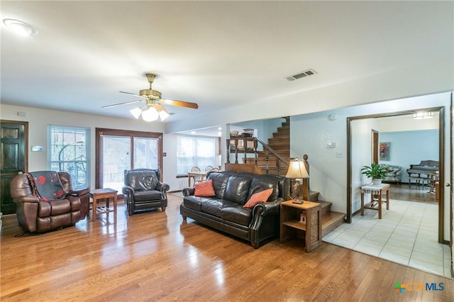 living area featuring stairs, light wood finished floors, visible vents, and a ceiling fan