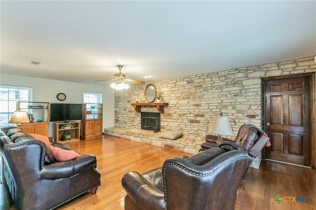 living area featuring a ceiling fan, visible vents, a fireplace, and wood finished floors