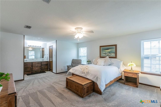 bedroom featuring a textured ceiling, light colored carpet, visible vents, baseboards, and ensuite bath