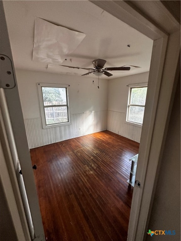 spare room featuring ceiling fan, wooden walls, a healthy amount of sunlight, and dark hardwood / wood-style floors