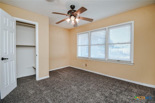 unfurnished bedroom featuring dark colored carpet, a textured ceiling, a closet, and ceiling fan