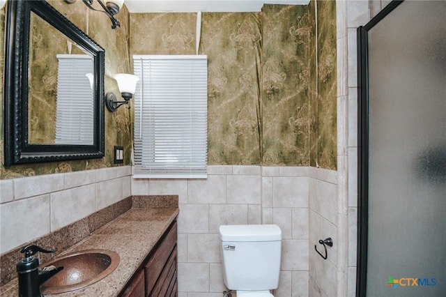 bathroom with a shower with shower door, tile walls, toilet, and vanity