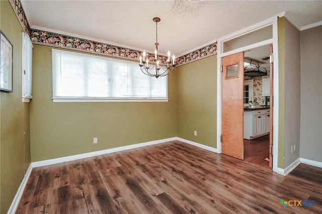 unfurnished dining area with a textured ceiling, dark hardwood / wood-style flooring, crown molding, and a notable chandelier