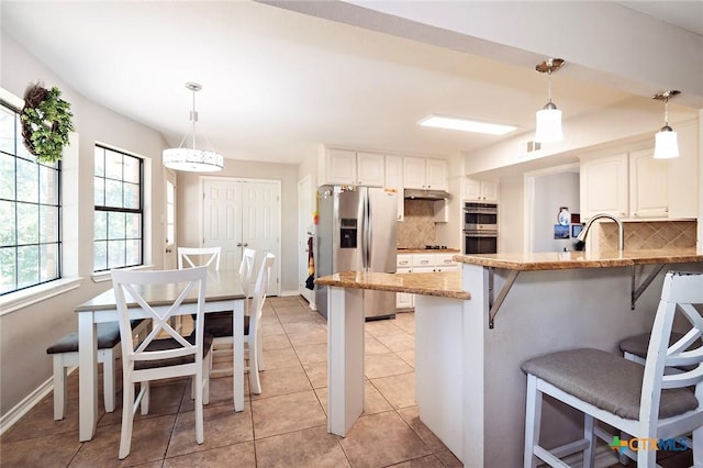 1104 Southridge, Salado, TX 76571 - kitchen with stainless steel appliances, tasteful backsplash, a kitchen bar, under cabinet range hood, and light stone counters