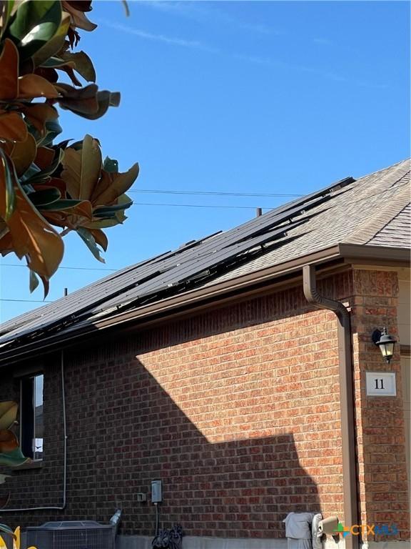 exterior details with central AC unit, gutters, brick siding, a downspout, and roof with shingles