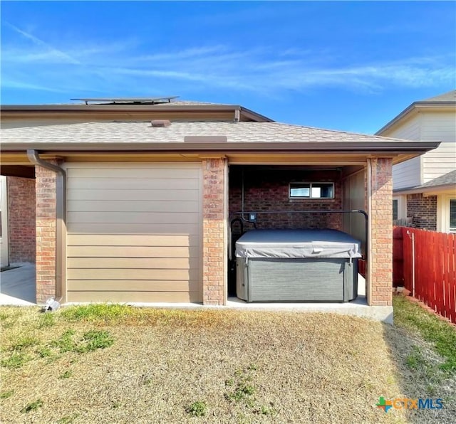 exterior space featuring a garage, brick siding, fence, roof with shingles, and a hot tub