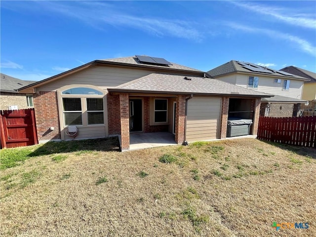 rear view of property with brick siding, fence, a lawn, roof mounted solar panels, and a patio area