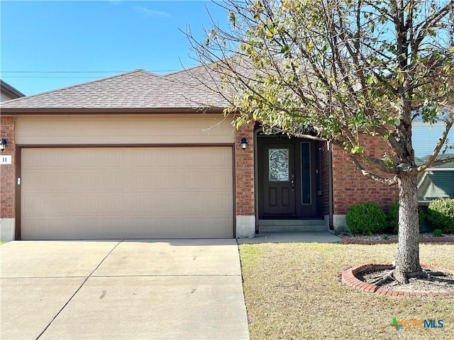 view of front of house featuring a garage, concrete driveway, brick siding, and roof with shingles