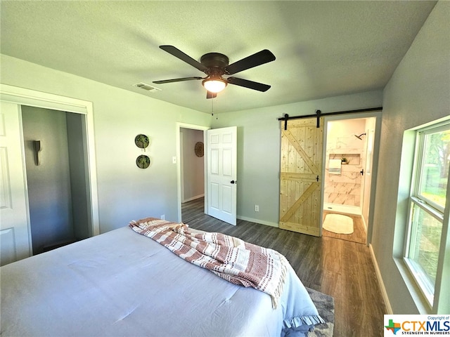 bedroom with dark hardwood / wood-style flooring, ensuite bath, a textured ceiling, ceiling fan, and a barn door