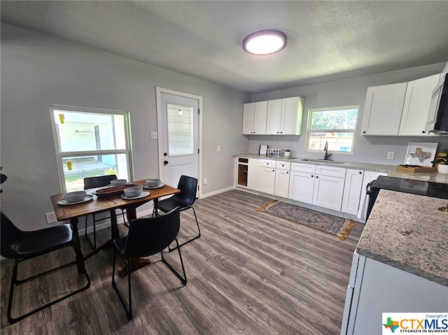 kitchen with black stove, dark hardwood / wood-style flooring, light stone counters, sink, and white cabinets