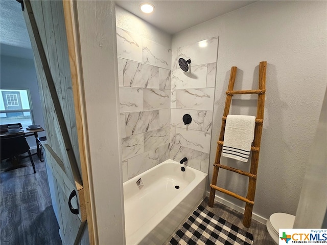 bathroom featuring hardwood / wood-style floors, tiled shower / bath combo, and toilet