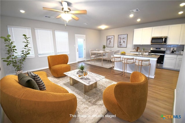 living area with light wood-type flooring, visible vents, baseboards, and recessed lighting