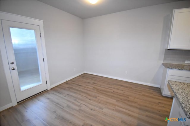 unfurnished dining area featuring light wood-type flooring, a healthy amount of sunlight, and baseboards