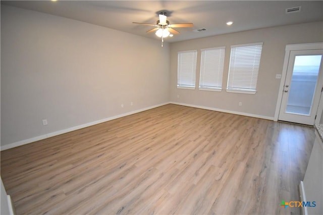 empty room with a ceiling fan, light wood-type flooring, visible vents, and baseboards