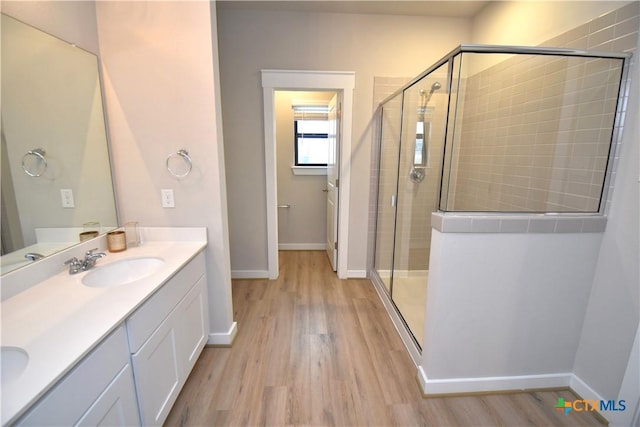 full bath featuring wood finished floors, a sink, baseboards, double vanity, and a stall shower