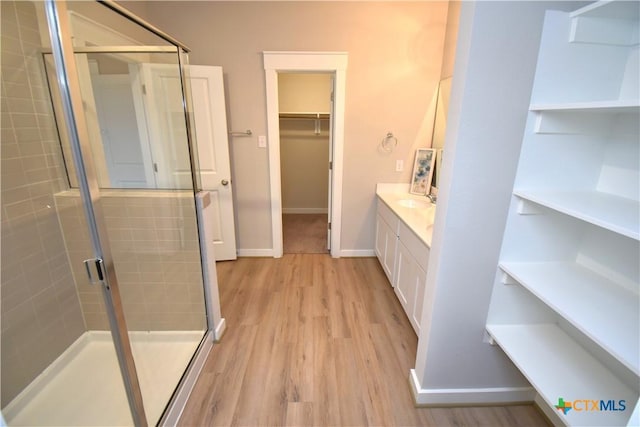 bathroom featuring a stall shower, baseboards, wood finished floors, a spacious closet, and vanity