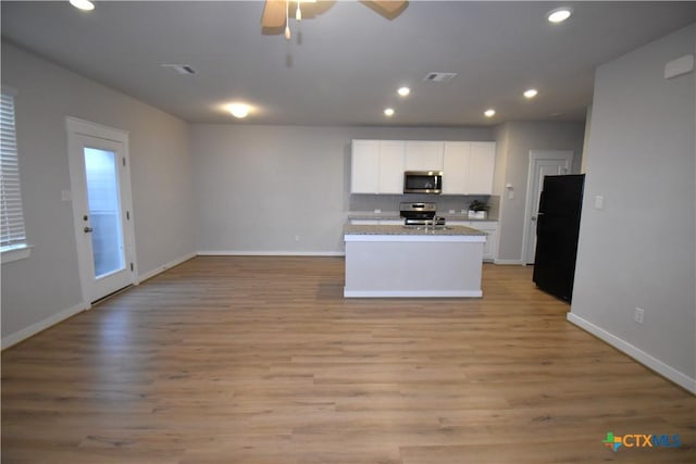 kitchen featuring light stone counters, white cabinets, open floor plan, appliances with stainless steel finishes, and light wood finished floors