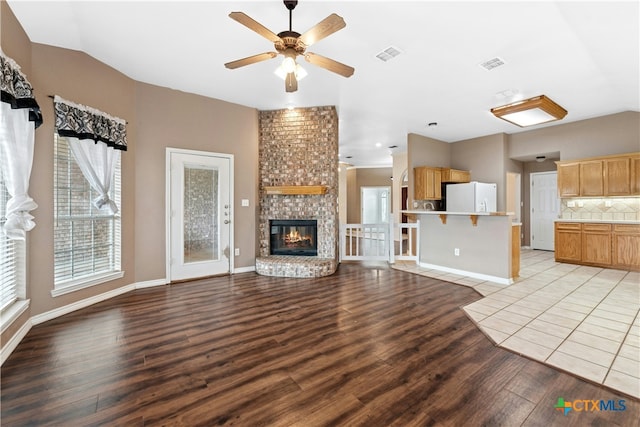 unfurnished living room with a ceiling fan, a fireplace, visible vents, and light wood-style floors